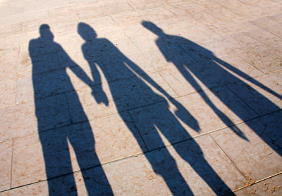 Schatten dreier Menschen, die sich an Hände halten und zusammen gehen.