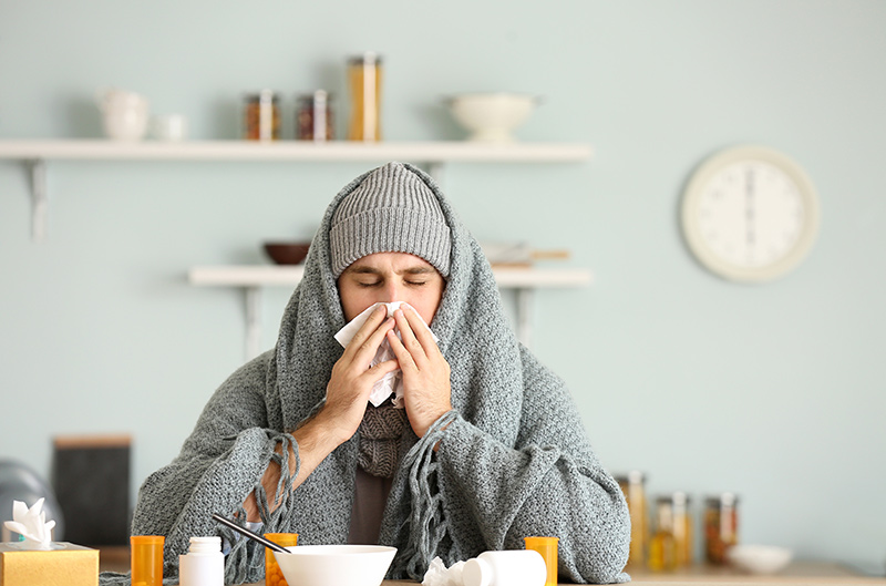Kranker Mann sitzt am Küchentisch und putzt seine Nase